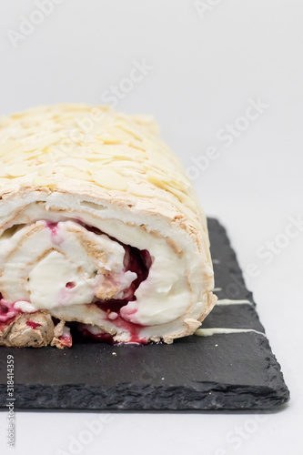 Meringue roll with white cream, red berries and nuts on a black tray on a white background photo