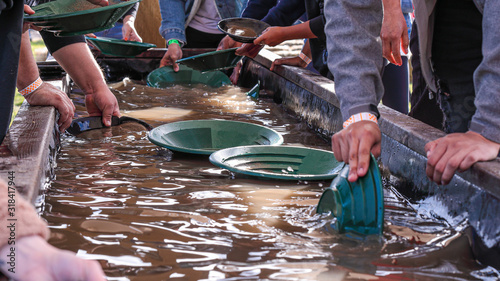 Foto People washing gold particles in a large wooden bath using green plastic plates