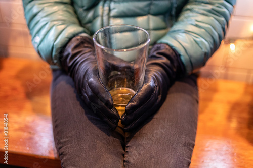 A woman in a black jeans, blue down jacket and leather gloves holding half empty beer glass