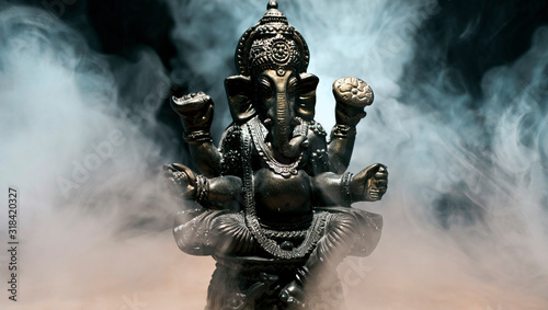 Hindu god Ganesha on black background. Statue with a smoke of incense. 