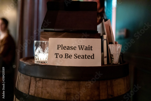 Posted sign on a hostess stand read " Please Wait to be seated"