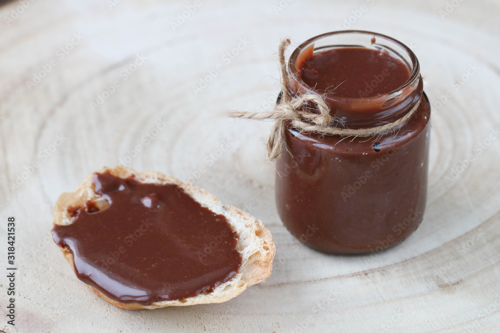 Open glass jar with some chocolate paste, chocolate spread on bread on light wooden background. Side view, copy space Open glass jar with some chocolate paste, chocolate spread on bread on light wooden background. Side view, copy space