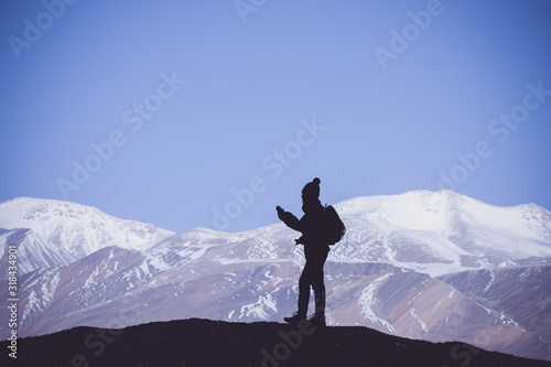 Tourist with backpack using smartphone on the rock in the beautiful mountains view of snowy Tso Moriri Lake in Leh Ladakh india, freedom concept