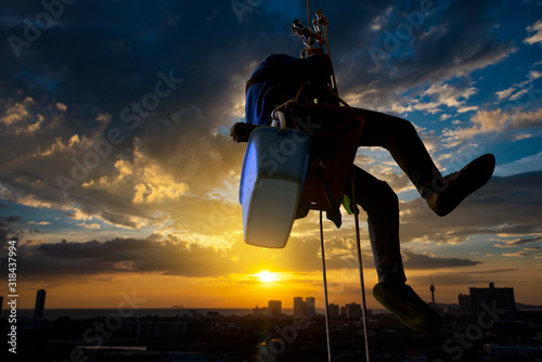 Silhouette  person window cleaner climbing hight risk building with safty equitment for cleaning window with sunset sky black cloud background. photo