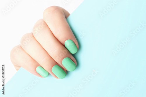 Female hand with trendy manicure Neo-mint on blue background with copy space
