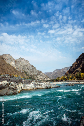 Mighty river flows along stony banks among rocky mountains against a clear blue sky. Turquoise water of stormy river and huge stones. Vertical image of beautiful natural landscape. © exebiche