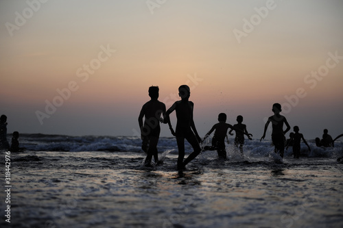 Silhouettes of children jumping in the surf on the background of the sea and evening sky. Boyish figures, children playing on seashore. Carefree childhood, concepts of freedom and the future.