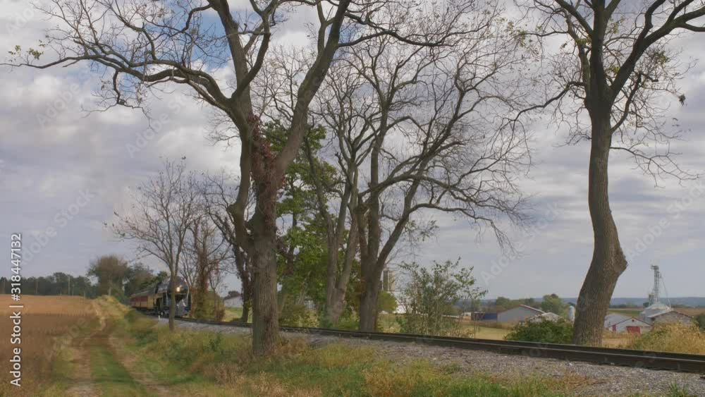 Head on view of an antique steam engine blowing black smoke pulling passenger cars thru countryside Head on view of an antique steam engine blowing black smoke pulling passenger cars thru countryside