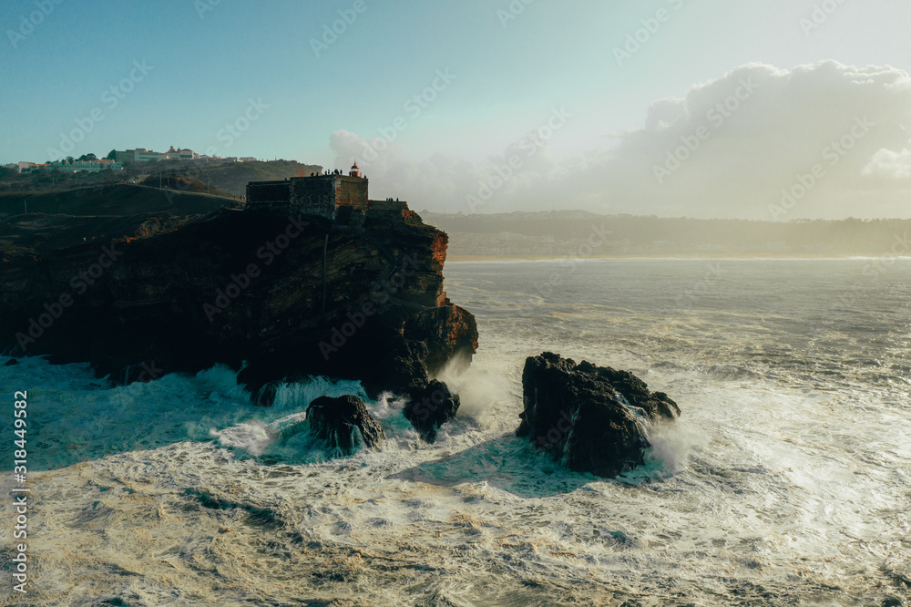 Nazare Portugal giant waves hitting cliffs rocks and lighthouse from above view drone