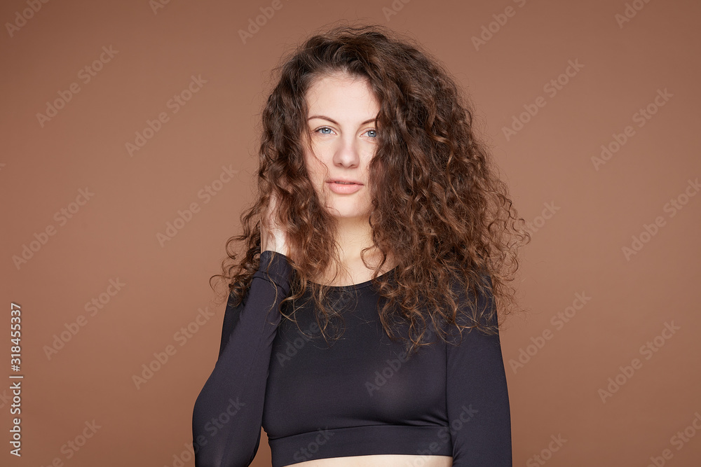 Indoor studio shot of beautiful curly haired woman with long hair, dressed in underwear, shows her perfect slim body, looks seriously at camera, has healthy skin. Young female isolated over beige wall Indoor studio shot of beautiful curly haired woman with long hair, dressed in underwear, shows her perfect slim body, looks seriously at camera, has healthy skin. Young female isolated over beige wall