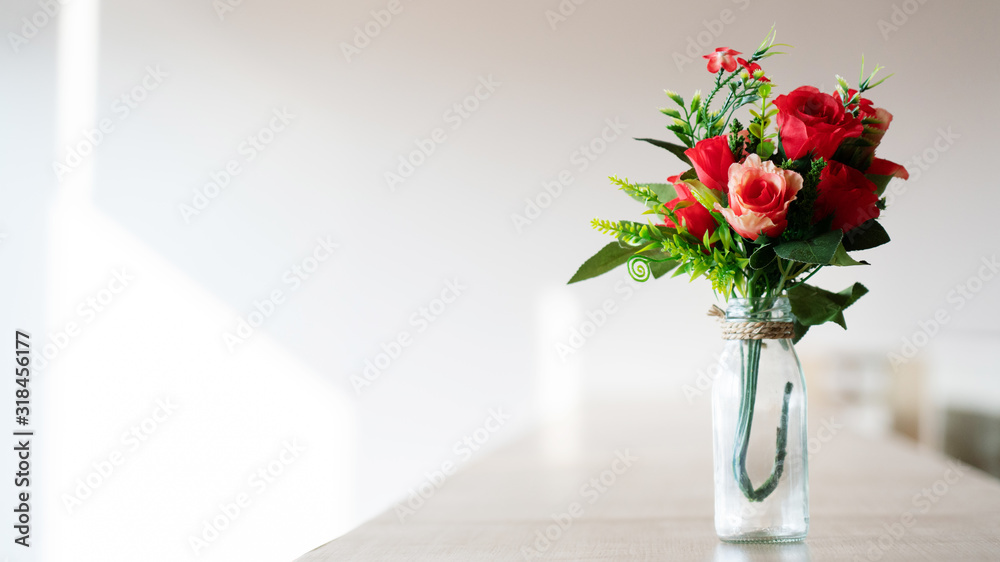 Bouquet of red plastic roses in a glass bottle placed on a wooden table. Wedding decorations, Valentine's day, home decorations Or office. Doing export business of fake flowers. copy space Bouquet of red plastic roses in a glass bottle placed on a wooden table. Wedding decorations, Valentine's day, home decorations Or office. Doing export business of fake flowers. copy space