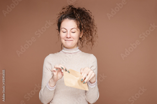 Negative human feelings, emotions concept. Mistrustful female opening craft paper jacket, feels upset, grimaces from fear, wears casual slim cashmere sweater, isolated on beige wall studio background.