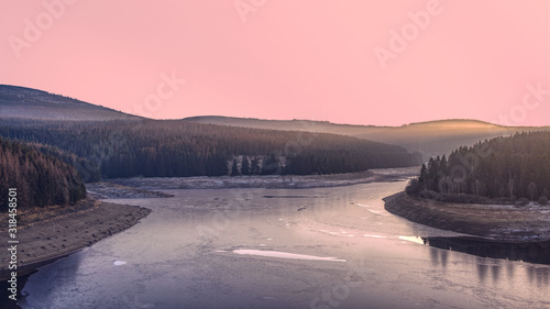Frozen dam in the winter forest at sunset. A pink illuminated sky above Ecker Reservoir and Ecker Dam near Bad Harzburg  Harz mountain range  Lower Saxony Saxony-Anhalt  Germany.