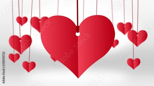 Red paper heart hanging on red string with other small hanging red hearts on white background