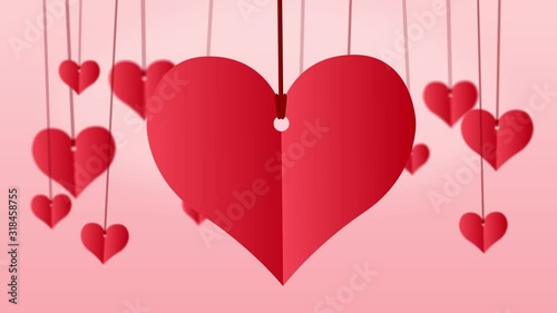 Red paper heart hanging on red string with other small hanging red hearts on pink background