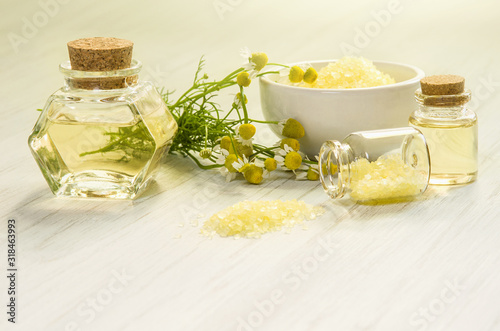 Pharmacy chamomile flower, water or infusion in glass bottles and bath or SPA salt on white wooden background