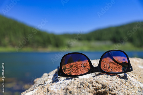 Polarized sunglasses on top of a rock by a lake