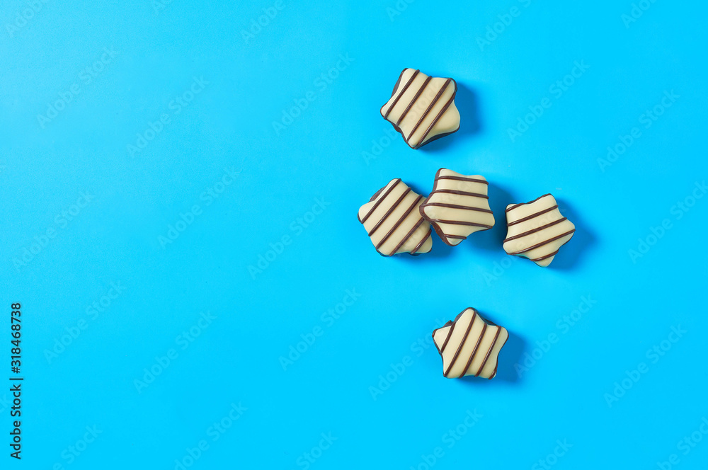 Scattered striped white and dark chocolate candies in shape of star lies on blue countertop. Space for text. Top view