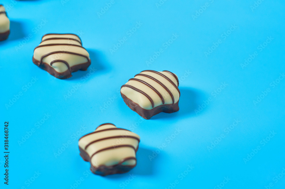 Scattered striped white and dark chocolate candies in shape of star lies on blue countertop. Close-up Scattered striped white and dark chocolate candies in shape of star lies on blue countertop. Close-up