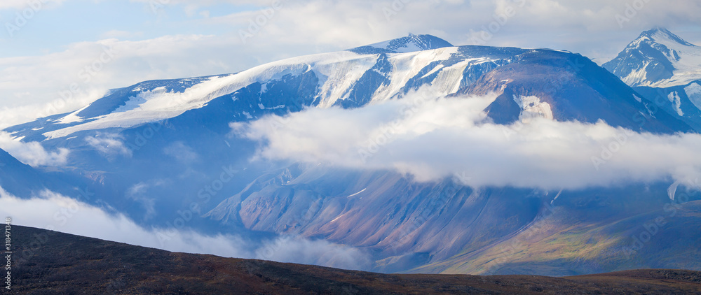 Snow-capped mountain peaks rise above the clouds. Panoramic view.