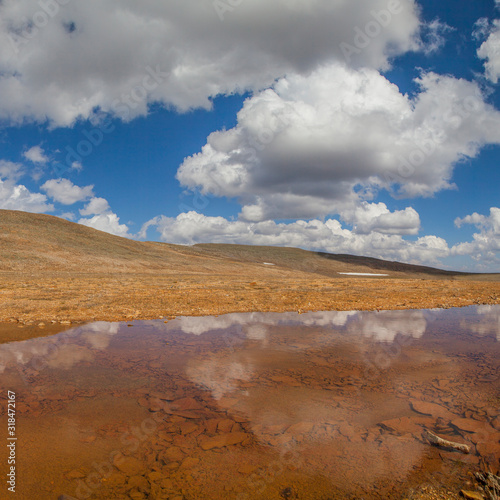Unusual lake with red water. Desert mountain slopes and picturesque sky.