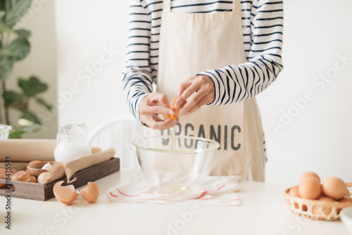 Male hands are breaking an egg into bowl to make dough on white table photo