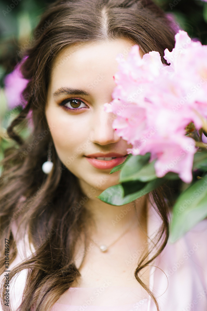 A beautiful young brunette with a smile and big brown eyes in blooming gardens of pink rhododendrons covered Godin's eye with a flower A beautiful young brunette with a smile and big brown eyes in blooming gardens of pink rhododendrons covered Godin's eye with a flower