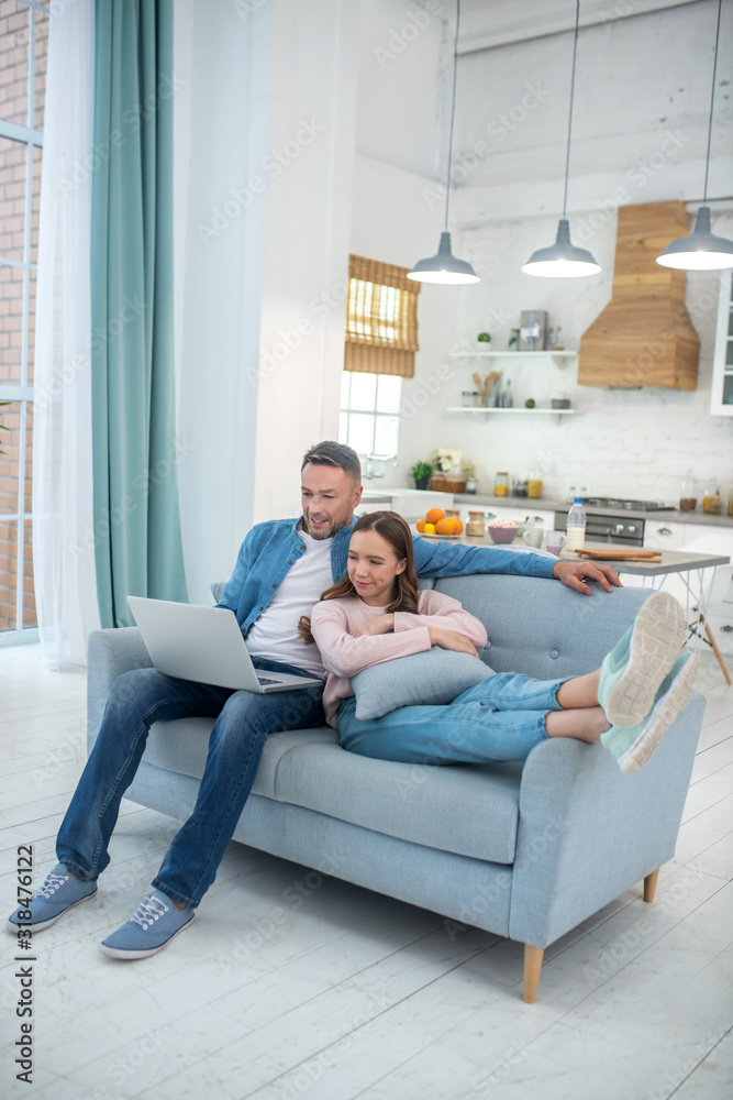 Fototapeta premium Daughter with father looking at laptop on sofa at home.