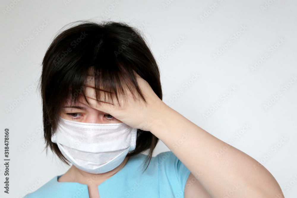 Sick woman in medical mask holds hand to her forehead. Concept of illness, fever, cold and flu, head pain, coronavirus symptoms
