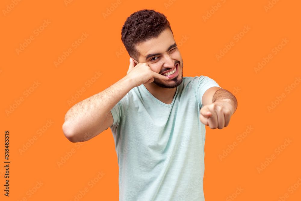 You contact us! Portrait of positive brunette man with beard in white t-shirt making gesture with fingers dial my number or call me back and pointing at you. studio shot isolated on orange background You contact us! Portrait of positive brunette man with beard in white t-shirt making gesture with fingers dial my number or call me back and pointing at you. studio shot isolated on orange background