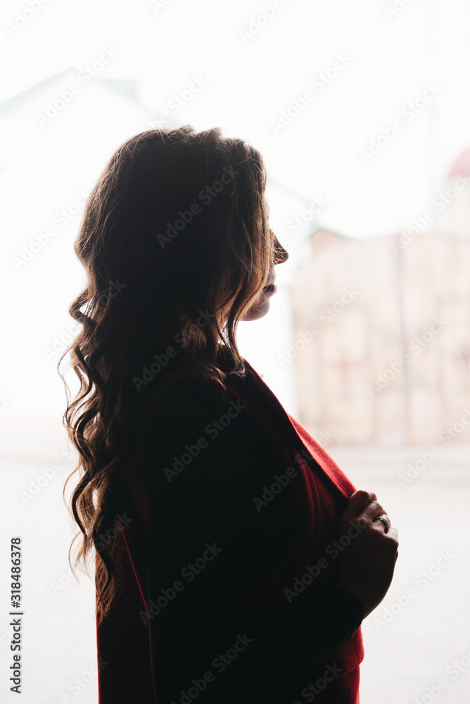 Outdoor portrait of a stylish young girl on the street of an old city in black clothes and a long red vest. Silhouette photo. A model poses on the street of a European city