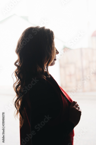 Obraz na płótnie Outdoor portrait of a stylish young girl on the street of an old city in black clothes and a long red vest. Silhouette photo. A model poses on the street of a European city w salonie