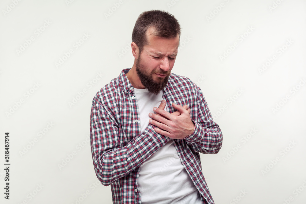 Heart attack, cardiological problems. Portrait of stressed out bearded man in plaid shirt grabbing chest suffering acute pain cramp, risk of infarct. indoor studio shot isolated on white background Heart attack, cardiological problems. Portrait of stressed out bearded man in plaid shirt grabbing chest suffering acute pain cramp, risk of infarct. indoor studio shot isolated on white background