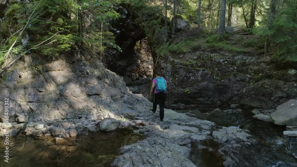 Active woman hiking walking over the rocks at a stream in the wildnerness looking at a natural bridge formed by nature. Active woman hiking walking over the rocks at a stream in the wildnerness looking at a natural bridge formed by nature.