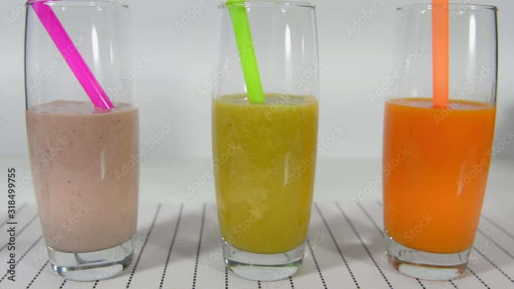 Dip a pink straw in a smoothie cocktail on a white background. Three tasty healthy cocktails on a white background. Dip a pink straw in a smoothie cocktail on a white background. Three tasty healthy cocktails on a white background.