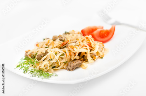 Stewed vegetables with meat: cabbage, onions, carrots and beef on a white plate on a white background