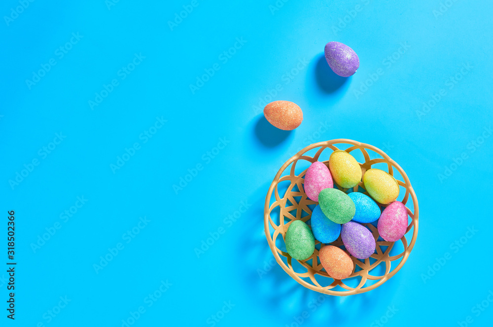 Full plastic basket of colorful eggs with glitters lies on blue table on kitchen. Easter concept. Space for text. Top view