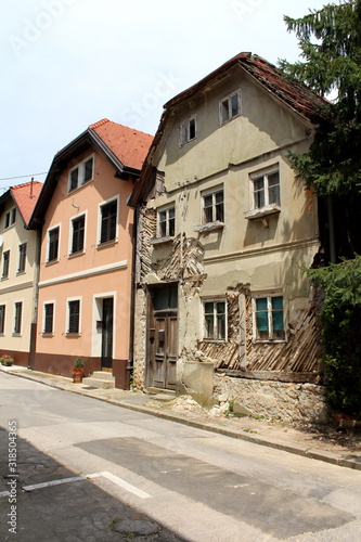Row of renovated attached old suburban family houses with one abandoned ruin at the end of street with dilapidated cracked walls and cracked wooden doors surrounded with paved road and tall trees