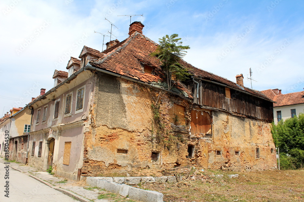 Obraz premium Ruins of large old abandoned suburban family house with destroyed cracked walls and boarded windows in old part of town surrounded with attached houses and paved road