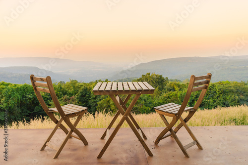Empty wooden table and chairs on terrace. Beautiful seating with landscape mountains view while sunset.