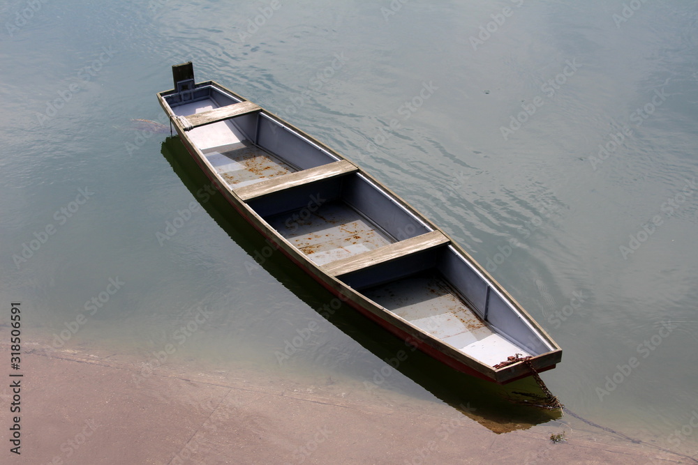 Wooden river boat made of dilapidated wooden boards with grey metal parts tied to concrete river bank with strong rusted chain surrounded with calm water