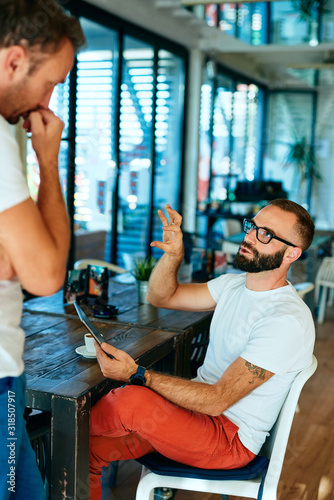 Attractive bearded man with glasses in a cafe working on laptop and chatting with a friend