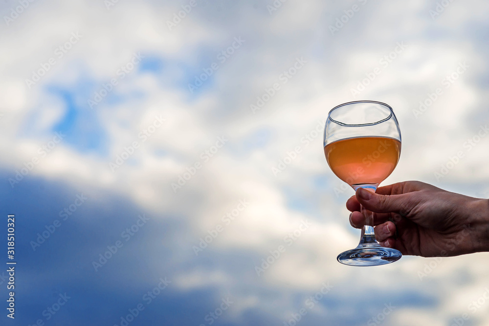 Glass with a drink in a woman's hand against the sky, free space.