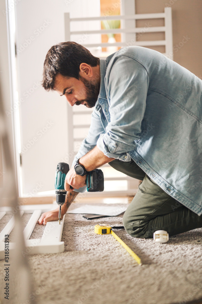 Man screwing baby crib with screwdriver machine.