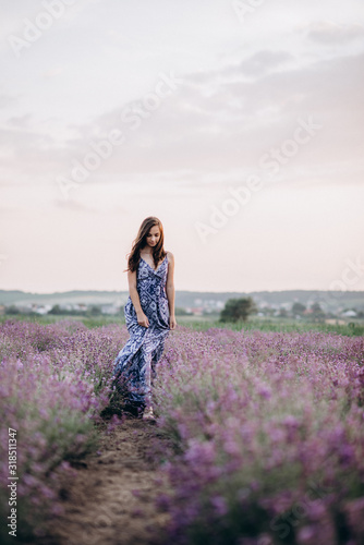 beautiful girl in a long dress walking in a lavender field at sunset. Soft focus.