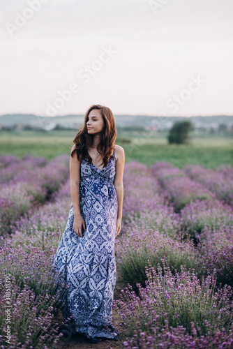 beautiful girl in a long dress walking in a lavender field at sunset. Soft focus.