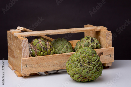 Sugar-apple or 'Fruta de Conde' [Earl Fruit] as it is known in Brazil in front of and part of an allotment in a small wooden crate as sold on the local market photo