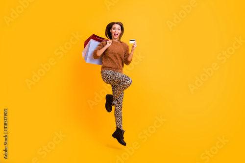 Full length profile photo of funny lady jump high carry packs shopaholic hold plastic credit card wear casual fluffy pullover leopard trousers boots isolated yellow color background