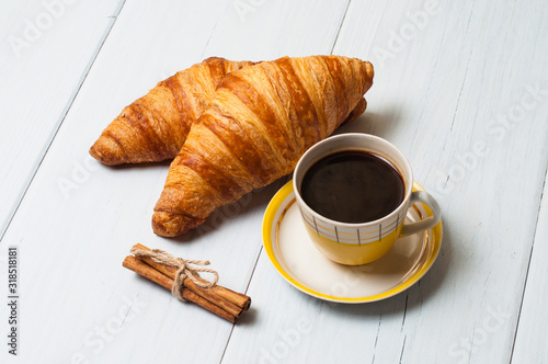 Espresso coffee in vintage yellow cup, croissants and cinnamon on a light background, breakfast concept