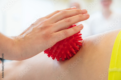 Eine weibliche Person massiert mit Hilfe eines roten Massageballs den Rücken einer Frau photo